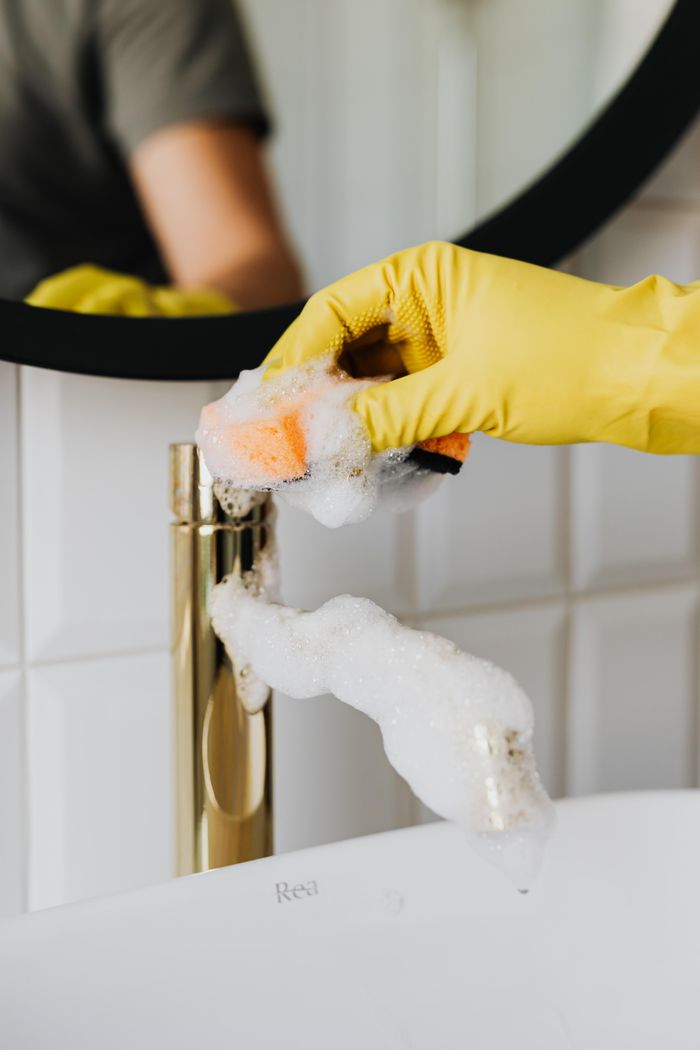 portfolio-01 Anonymous person washing golden shiny faucet and sink in bathroom while wearing yellow latex glove during household care routine work