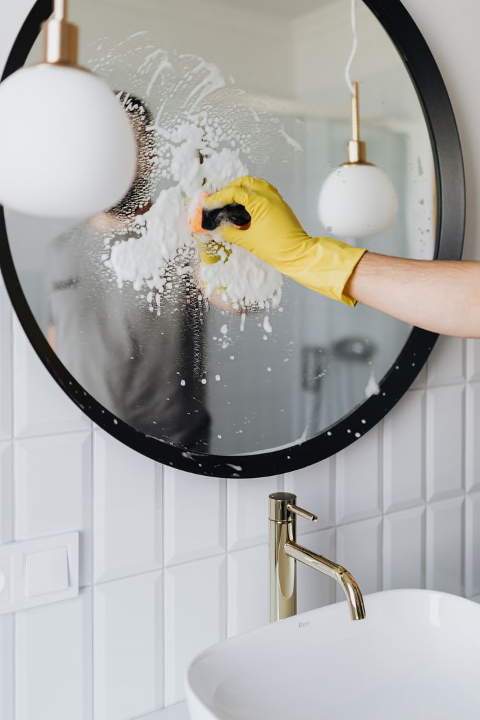 why-choose-us Anonymous housekeeper in yellow rubber gloves wiping round mirror by sponge in bathroom