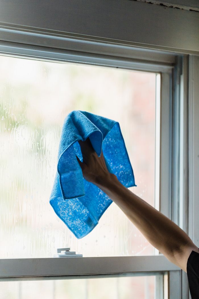portfolio-02 A hand using a blue towel to clean a window indoors, showcasing housework.